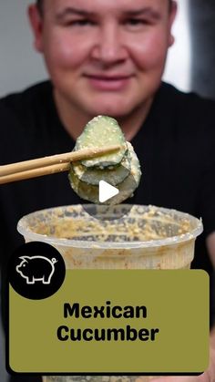 a man is holding up a cup filled with mexican cucumber and chopsticks