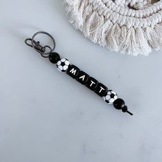 a black and white keychain with the word mat on it next to a tassell