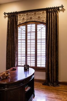 a living room with wooden floors and large window covered in brown drapes next to a coffee table