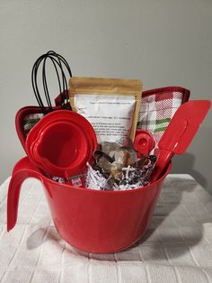 a red bucket filled with kitchen items on top of a white tablecloth covered table