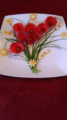 a white plate topped with red flowers on top of a red tablecloth covered floor