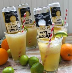 four glasses filled with drinks sitting on top of a table next to oranges and limes