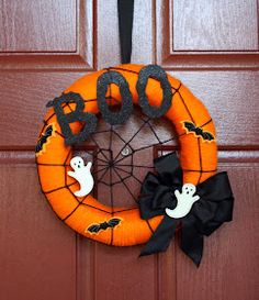 an orange wreath with black ribbon and ghost decorations hanging on the front door for halloween