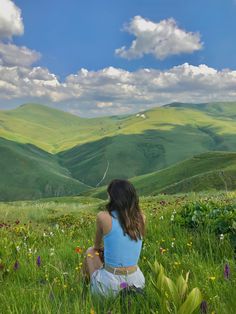 a woman sitting in the grass looking at mountains