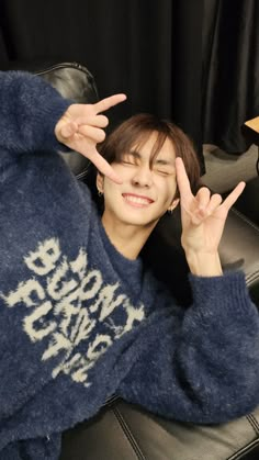 a person sitting in a chair making the peace sign with their hands while wearing a blue sweater