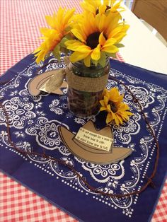 sunflowers are placed in a mason jar on a blue tablecloth with a red and white checkered table cloth