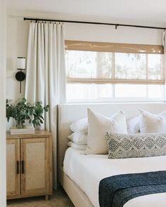 a bed with white sheets and pillows in a bedroom next to a wooden cabinet under a window