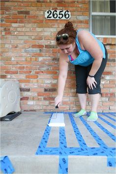 a woman in blue shirt and black shorts painting a brick wall with white paint on it