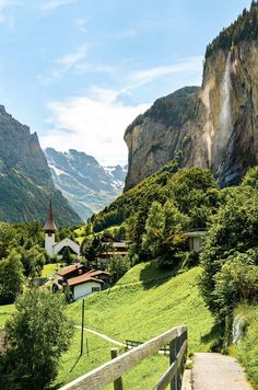 a wooden path leading to a village in the middle of a valley with mountains behind it