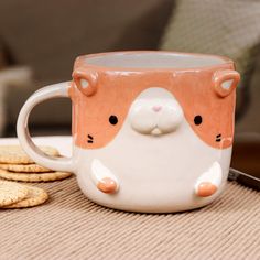 a coffee mug with a cat face on it next to crackers and a cell phone