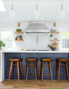 three wooden stools sit in front of an island with built - in hood and shelves