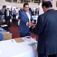 two men in suits are talking to each other at a business event with people standing around