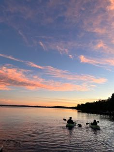 three people in kayaks paddling on the water at sunset or dawn with pink clouds