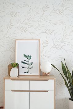 a white dresser topped with a plant next to a potted plant and a framed photo