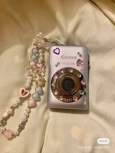 a camera is laying on top of a bed with pearls and beads attached to it