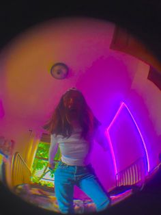 a girl in white shirt and blue jeans standing next to a pink neon light tunnel