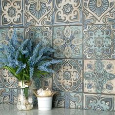 a vase with some blue flowers in it on a counter next to a tile wall