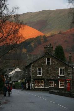 people are walking down the street in front of some buildings with mountains in the background