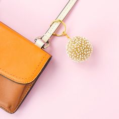 an orange purse with a white beaded ball hanging from it's front pocket