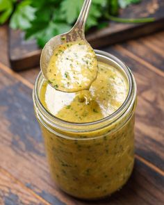 a spoon full of pesto sauce sitting on top of a wooden table next to parsley