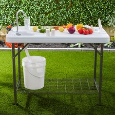 a white table topped with a bucket of fruit next to a sink and faucet