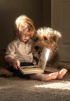 a little boy sitting on the floor reading a book to a dog