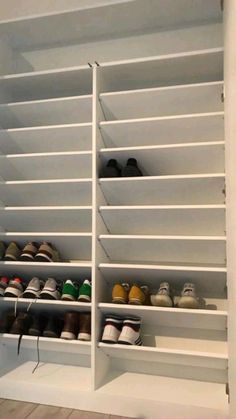 a white shelf filled with lots of shoes on top of wooden floor next to a wall