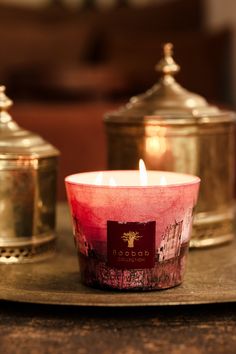 a lit candle sitting on top of a table next to two gold covered containers with candles in them