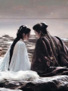 two women dressed in traditional japanese clothing sitting on rocks looking at each other with water behind them