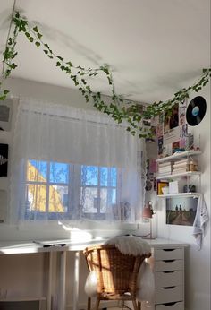 a room with a desk, chair and plants hanging from the ceiling over it's windows