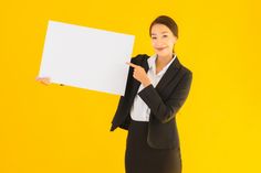 a woman in a business suit holding up a white board with one hand and pointing at it