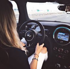 a woman driving a small car down a road with her hands on the steering wheel