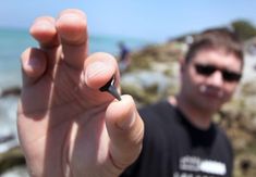 a man is holding up his black pen in front of the camera while standing next to the ocean