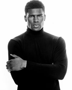 a man in a black turtle neck shirt is posing for a photo with his arms crossed