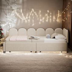 a white bed sitting under a christmas tree next to a wall with lights on it