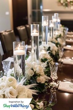 the table is set with candles, flowers and glass vases for centerpieces