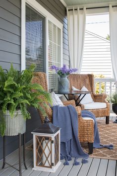 a porch with wicker chairs and plants on the side walk, along with a blue blanket