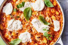 a pan filled with pasta and cheese on top of a wooden table next to basil leaves