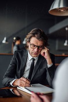 a man in a suit and tie sitting at a table writing on a piece of paper