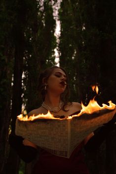 a woman is holding a book with flames in her hands while she looks up at the sky