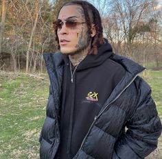 a man with dreadlocks and tattoos on his face standing in the grass wearing a black jacket