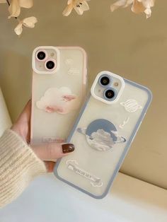 two iphone cases with stickers on them are held up in front of a flower