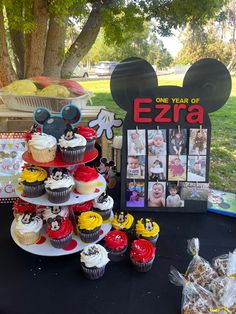 mickey mouse cupcakes are stacked on top of each other in front of a sign that says, one year of ezra