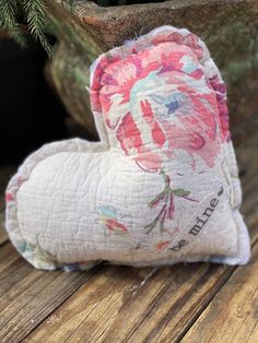 a flowered heart shaped pillow sitting on top of a wooden table next to a potted plant