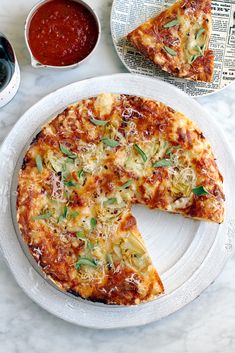 a white plate topped with a pizza next to a slice of pizza