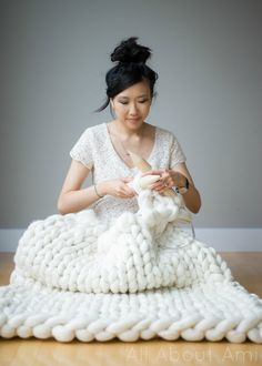 a woman is knitting a blanket on the floor with a yarn ball in front of her