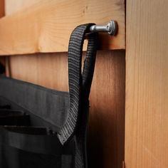 a black bag hanging on the side of a wooden wall next to a metal hook