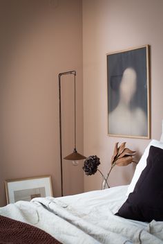 a bedroom with pink walls and white linens on the bed, framed artwork above