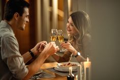 two people sitting at a table with wine glasses in their hands and plates on the table