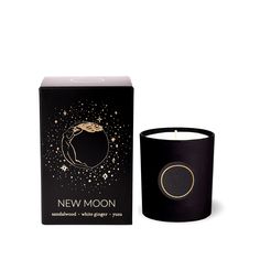 a candle that is next to a box on a white background with the words new moon written in gold